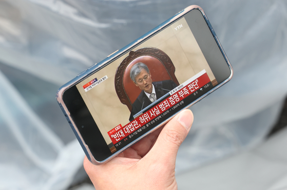 1일 서울 중구 숭례문 인근에서 민주노총 주최로 열린 2025 세계노동절대회에서 한 참가자가 더불어민주당 이재명 대선 후보의 공직선거법 사건에 대한 대법원 판결 생중계를 휴대전화로 보고 있다. 연합뉴스