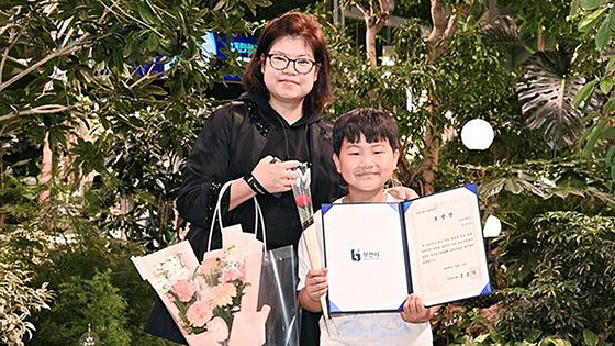 모범 어린이 표창장을 들고 웃고 있는 정태운군과 정군의 어머니. 사진 부천시