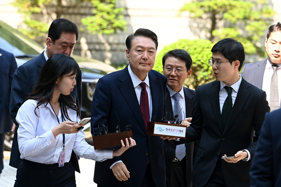 윤석열 전 대통령이 12일 오전 내란 및 직권남용 혐의 사건 재판에 출석하기 위해 서울 서초구 중앙지방법원에 도착해 취재진의 질문을 받으며 이동하고 있다. 윤 전 대통령은 이날 처음으로 법원 지상으로 출석했지만, 포토라인에 멈춰 서지 않고 말없이 법원 청사로 들어갔다. [사진 사진공동취재단]