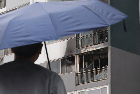 지난 24일 오전 부산진구의 한 아파트 화재 현장에서 한 시민이 우산을 쓰고 지나고 있다. 송봉근 기자