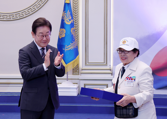 이재명 대통령이 27일 청와대 영빈관에서 열린 '호국 보훈의 달, 대통령의 초대' 행사에서 특별 초청대상자인 이춘자 씨에게 광목이불을 선물한 뒤 박수치고 있다.연합뉴스