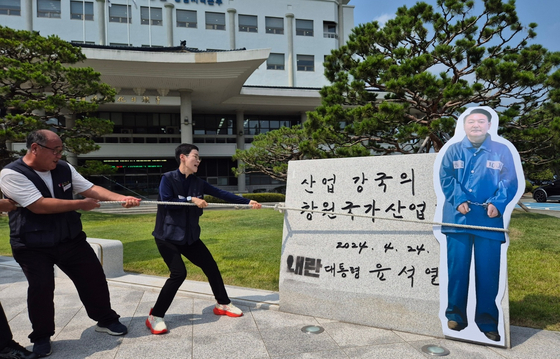 윤석열 전 대통령 친필 휘호 표지석을 훼손한 혐의로 민주노총 경남본부 소속 40대 A씨가 검찰에 송치되자 지역 노동계가 8일 경남 창원시 성산구 한국산업단지공단 경남지역본부 앞마당에 설치된 이 표지석을 밧줄로 묶고 잡아당기는 퍼포먼스를 하고 있다. 연합뉴스