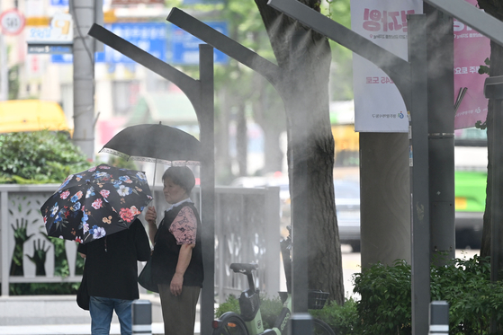 폭염특보가 이어지고 있는 지난 8일 오후 광주 동구 금남로에서 시민들이 양산을 쓴 채 쿨링포그가 뿜어내는 물안개를 맞고 있다. [뉴시스]