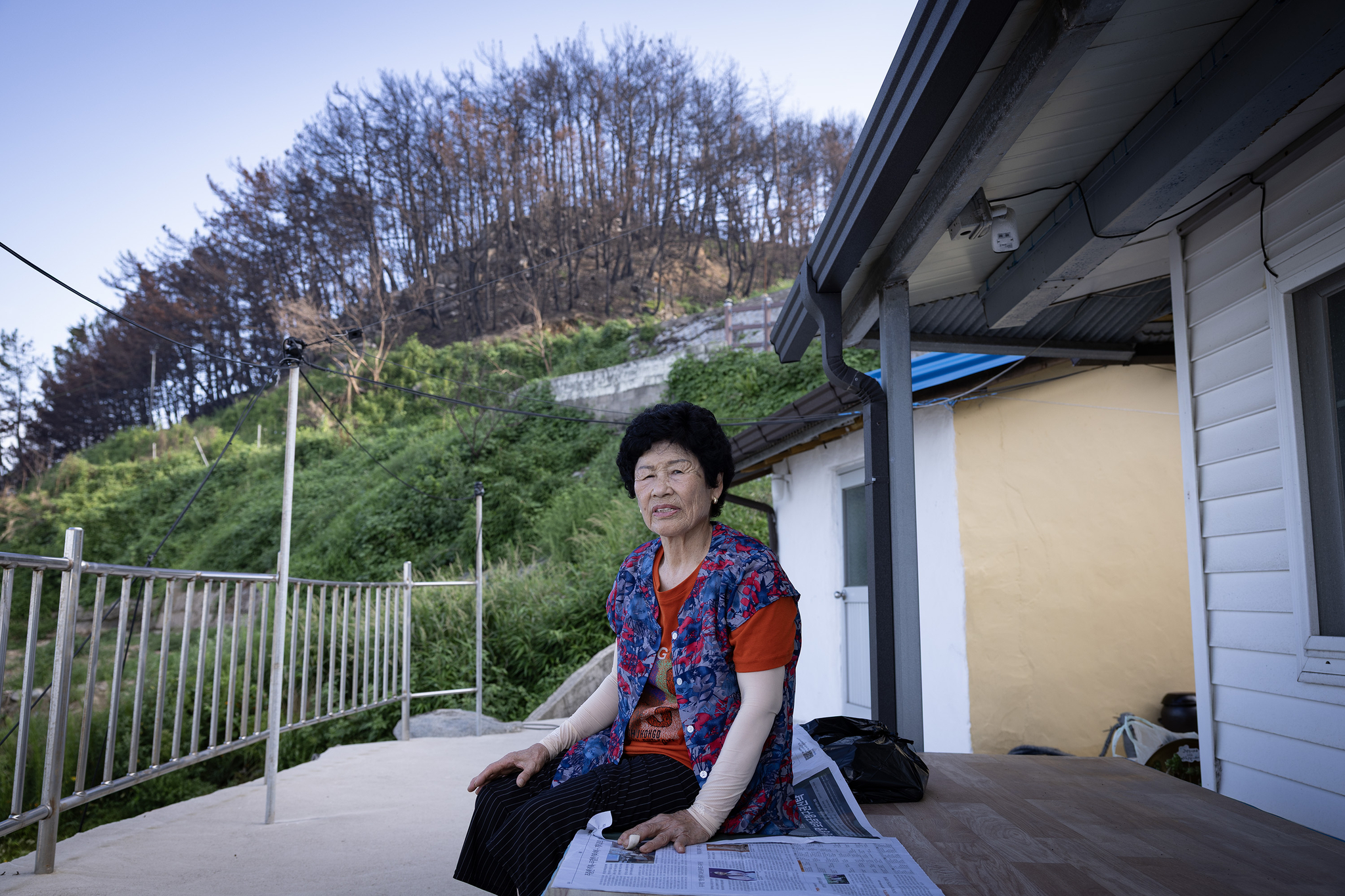 전정영 할머니가 본인의 집 마당 평상에 앉아 주변을 둘러보고 있다. 전 할머니 뒤로 불에 탄 산이 보인다. 불에 탄 나무의 뿌리가 약해져 산사태 위험이 있어 전 할머니도 이재민으로 살아가고 있다. 전민규 기자 
