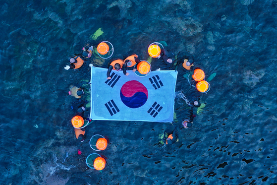 8일 오전 제주 해녀들과 울릉 해녀 등 10여명이 독도 몽돌해안 앞에서 물질 시연을 한 후 대형 태극기를 펼쳐 보이고 있다. 제주도 제공
