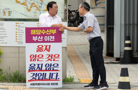 최민호 세종시장이 정부세정청사에 입주한 해양수산부 정문 앞에서 '해수부 부산 이전은 옳지 않다'는 피켓을 들고 1인 시위를 하고 있다. 최 시장이 출근길에 만난 해수부 노조사무총장과 악수하고 있다. 연합뉴스