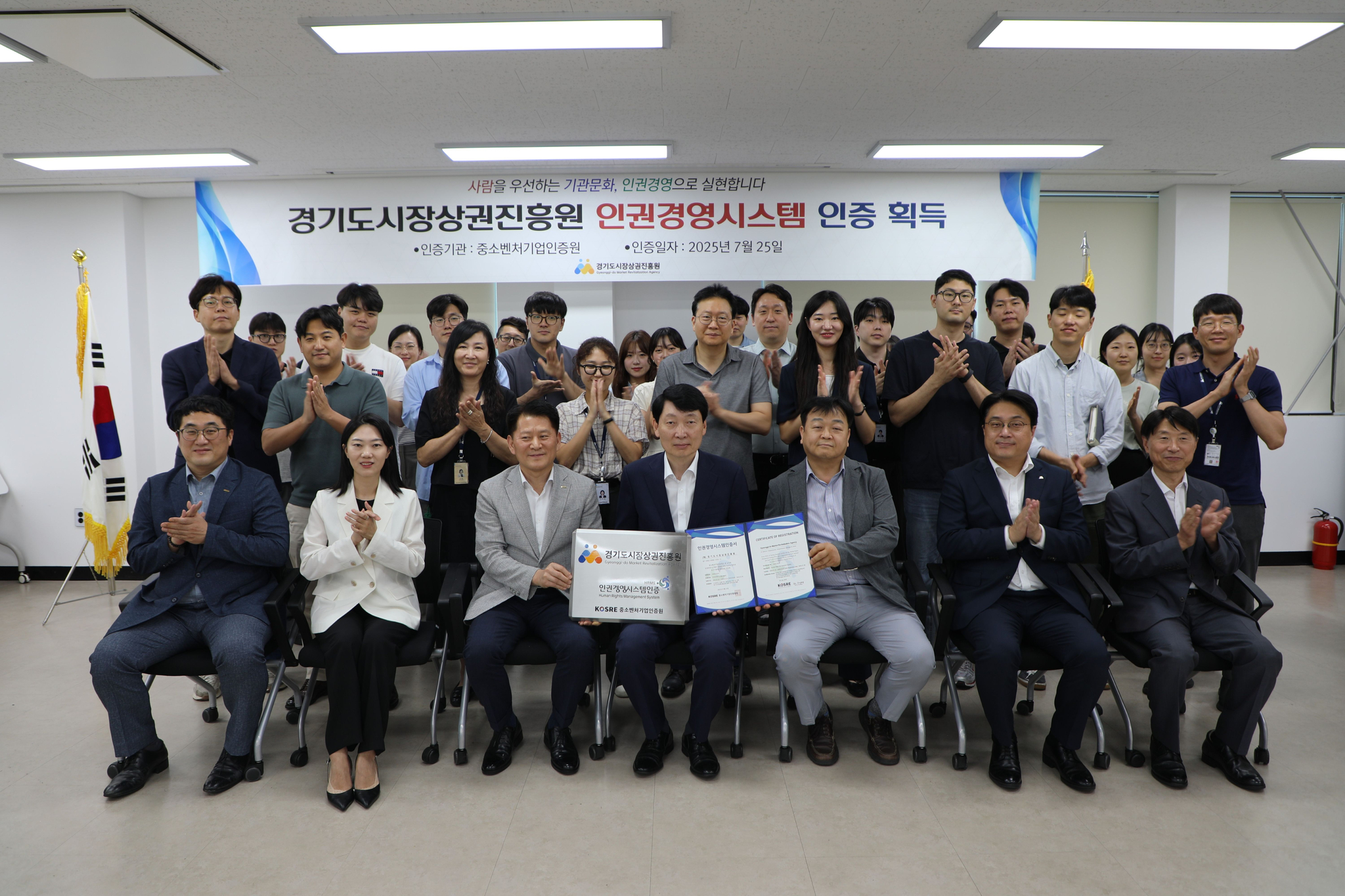 중소벤처기업인증원 엄진엽 원장과 경기도시장상권진흥원 김민철 원장이 경기도시장상권진흥원 임직원들과 함께 인권경영시스템 인증서 및 인증 현판 수여식 후 기념촬영을 하고 있다.