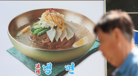 서울 마포구의 한 식당에 붙은 냉면 메뉴 사진 앞으로 시민이 지나고 있다.   연합뉴스