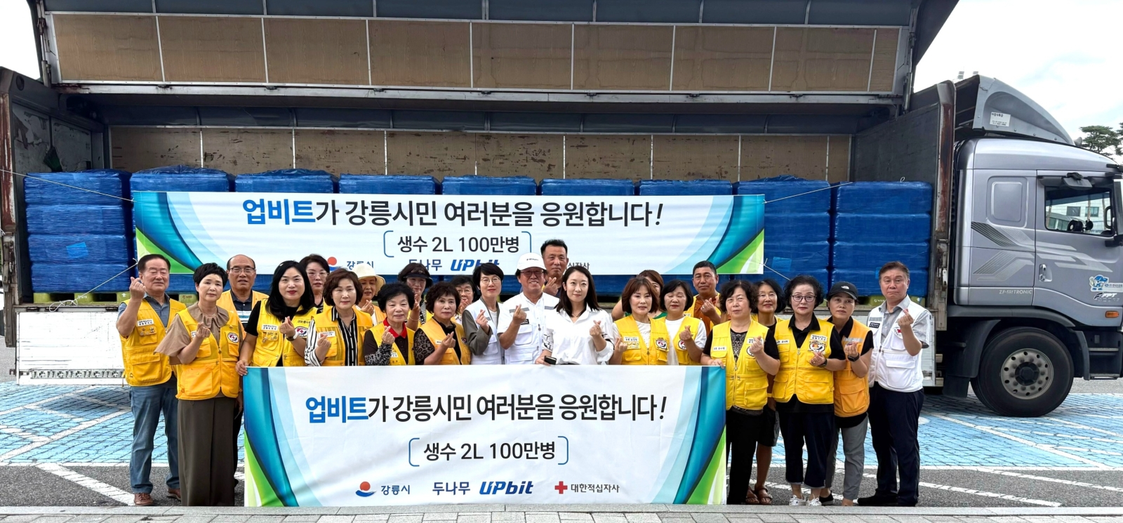 업비트가 강릉시에 생수 100만병을 기부, 대한적십자사 강릉지구봉사원 관계자들과 함께 기념 촬영을 하고 있다.