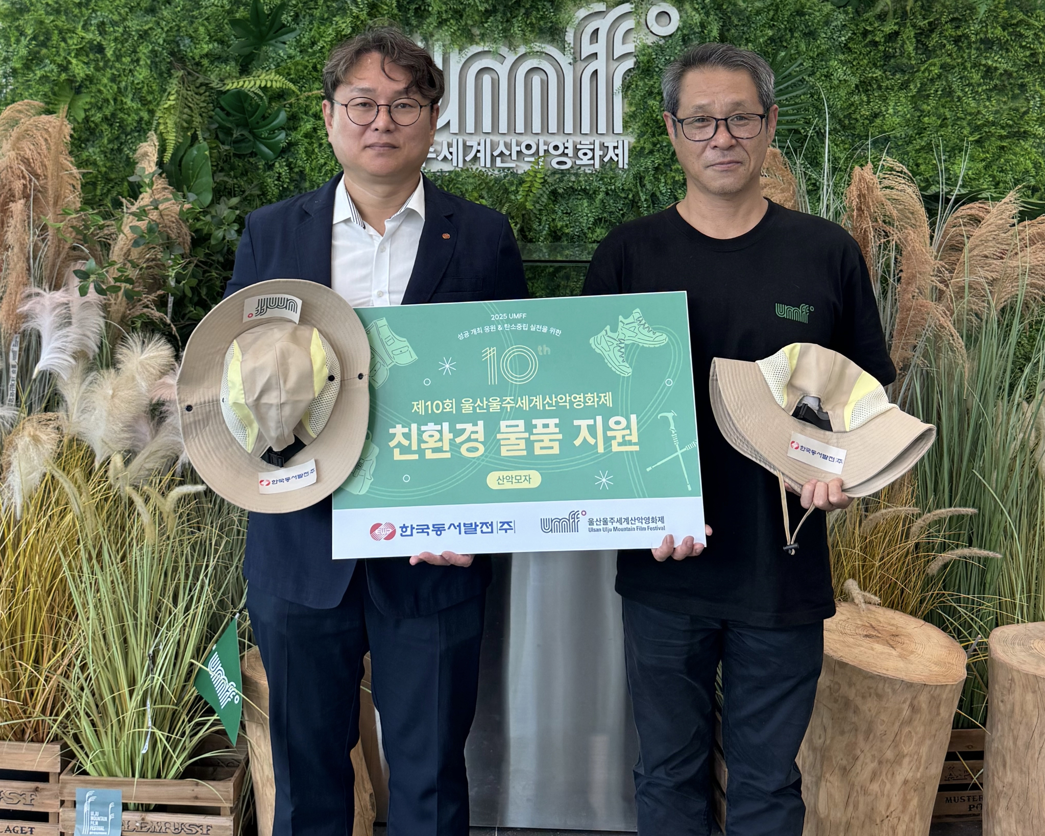 한국동서발전 사회공헌부 김태준 부장(왼쪽)과 울산울주세계산악영화제 홍영주 사무국장(오른쪽)이 친환경 모자를 전달하며 기념사진을 찍고 있다.