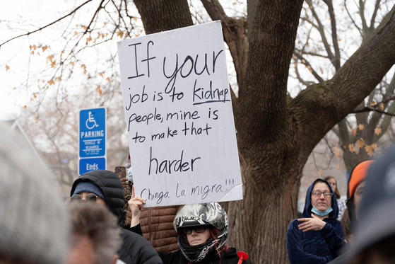 추수감사절 연휴을 앞둔 25일(현지시간) 미국 미네소타주 세인트폴에서 연방 이민국 요원들이 한 가정을 급습하는 가운데 한 시위자가 플래카드를 들고 있다. 로이터=연합뉴스