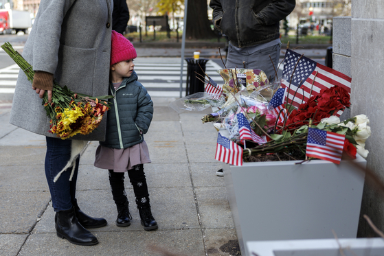 지난달 28일 미국 워싱턴DC 백악관 인근 교차로에서 한 어린이가 같은 달 26일 주방위군 소속 병사 앤드루 울프와 사라 벡스트롬이 아프가니스탄 출신 라마눌라 라칸왈이 쏜 총에 맞은 현장에 놓여져 있는 추모화와 미국 국기를 바라보고 있다. EPA=연합뉴스