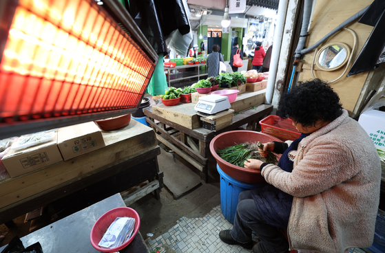 경기 수원시 팔달구 못골시장에서 상인들이 전기난로에 몸을 녹이며 파를 다듬고 있다. [뉴스1]