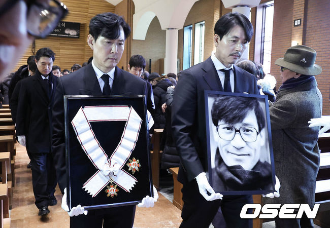 [OSEN=사진팀] 故 안성기 장례 미사 및 영결식이 9일 서울 명동성당에서 엄수됐다.안성기는 지난 5일 오전 9시 서울 용산구 순천향대병원 중환자실에서 치료를 받던 중 가족들이 지켜보는 가운데 향년 74세로 세상을 떠났다. 지난달 30일 자택에서 음식물이 목에 걸린 채 쓰러져 병원으로 이송된 뒤 의식불명 상태로 치료를 받아온 지 6일 만이다.영결식에서는 고인의 마지막 소속사 아티스트컴퍼니의 수장인 정우성과 이정재가 각각 영정과 훈장을 들며 고인을 배웅했다. 운구는 설경구, 박철민, 유지태, 박해일, 조우진, 주지훈이 맡았다.배우 정우성, 이정재가 영정과 금관문화훈장을 들고 운구 행렬과 영결식장을 나서고 있다. 2026.01.09 / photo@osen.co.kr사진=사진공동취재단