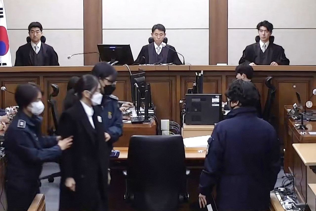 통일교 금품 수수 등 혐의로 구속기소된 김건희 여사가 28일 오후 서울중앙지방법원에서 열린 1심 선고 공판에 교도관들에게 양팔을 잡혀 출석하고 있다. 이날 김 여사의 선고 공판은 실시간으로 생중계됐다. 전 영부인에 대한 선고 공판 생중계는 이번이 처음이다. [사진 중앙지법 영상 캡처]