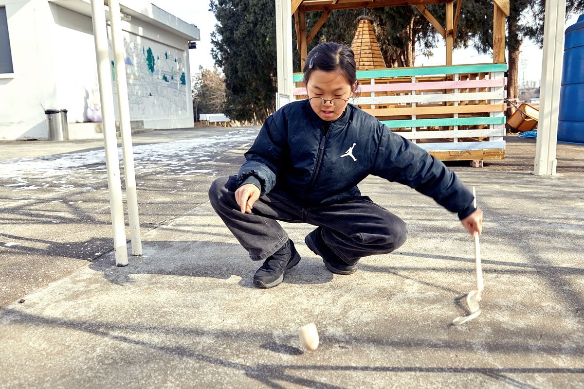 웃다리문화촌 건물 야외에 마련된 전통놀이 중 팽이치기를 즐긴 이한호 학생기자. 