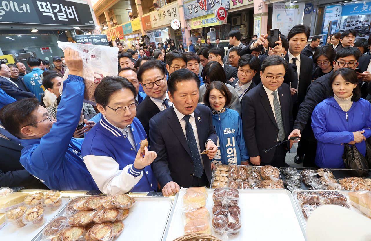 정청래 더불어민주당 대표(가운데)가 23일 오후 경남 양산시 중부동 양산남부시장에서 찹쌀도넛을 먹고 있다. 왼쪽은 김경수 경남지사 후보. 연합뉴스