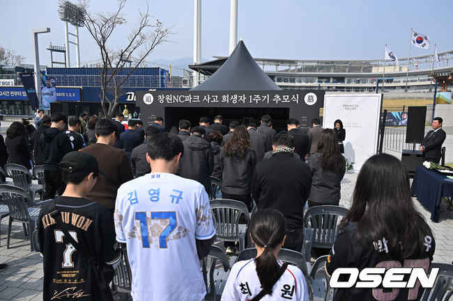 [OSEN=창원, 이석우 기자] 29일 창원NC파크에서 2026 신한 SOL KBO 리그 NC 다이노스와 두산 베어스의 경기가 열린다. 경남 창원시가 1년전 창원NC파크 화합의 탑 옆에서 외벽 구조물 추락 사망 사고 1주기 추모행사를 열었다. 참석한 시민과 NC 팬들이 희생자의 명복을 비는 묵념을 하고 있다. 2026.03.29 / foto0307@osen.co.kr