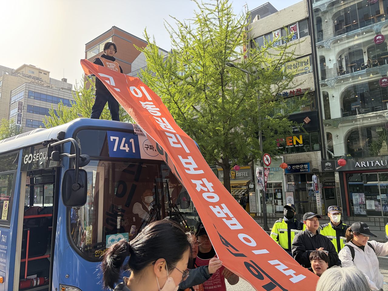 지난 달 21일 서울 종로2가 일대에서 열린 전국장애인차별철폐연대(전장연)의 이동권 보장 촉구 시위에서 한 참가자가 버스 위에 올라 현수막을 펼쳐 들고 있다.연합뉴스