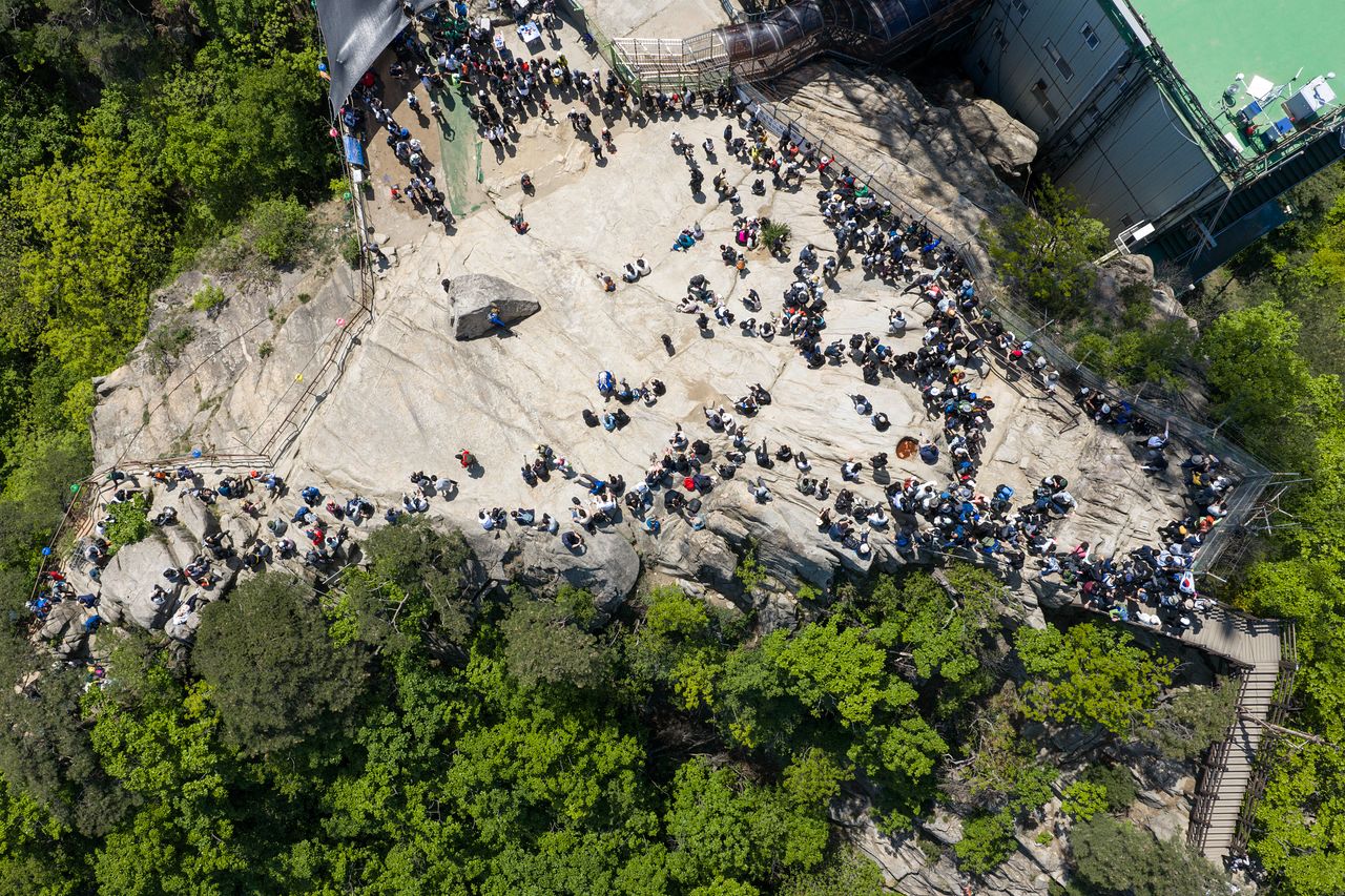 지난 1일 서울 관악산 정상에 인파가 몰려 있다. 등산객들은 인증샷을 찍은 뒤 정상석 뒤에서 다시 줄을 한바퀴 만들어 정상석 오른쪽으로 하산하고 있다. 정상석 뒤의 바위 웅덩이 '매염정(사진 가운데에서 조금 오른쪽 주황색 부분)'은 오염된 상태였다. 김정훈 기자. 