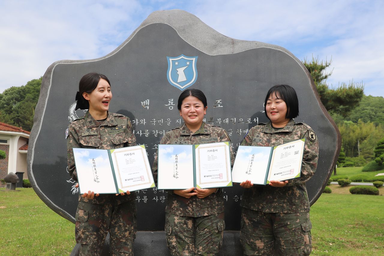 육군 32보병사단 노지희 상사(왼쪽), 홍윤경 하사(중앙), 최민지 중사가 기부 증서를 들고 부대 상징물 앞에서 사진을 찍고 있다. 사진 육군32보병사단 