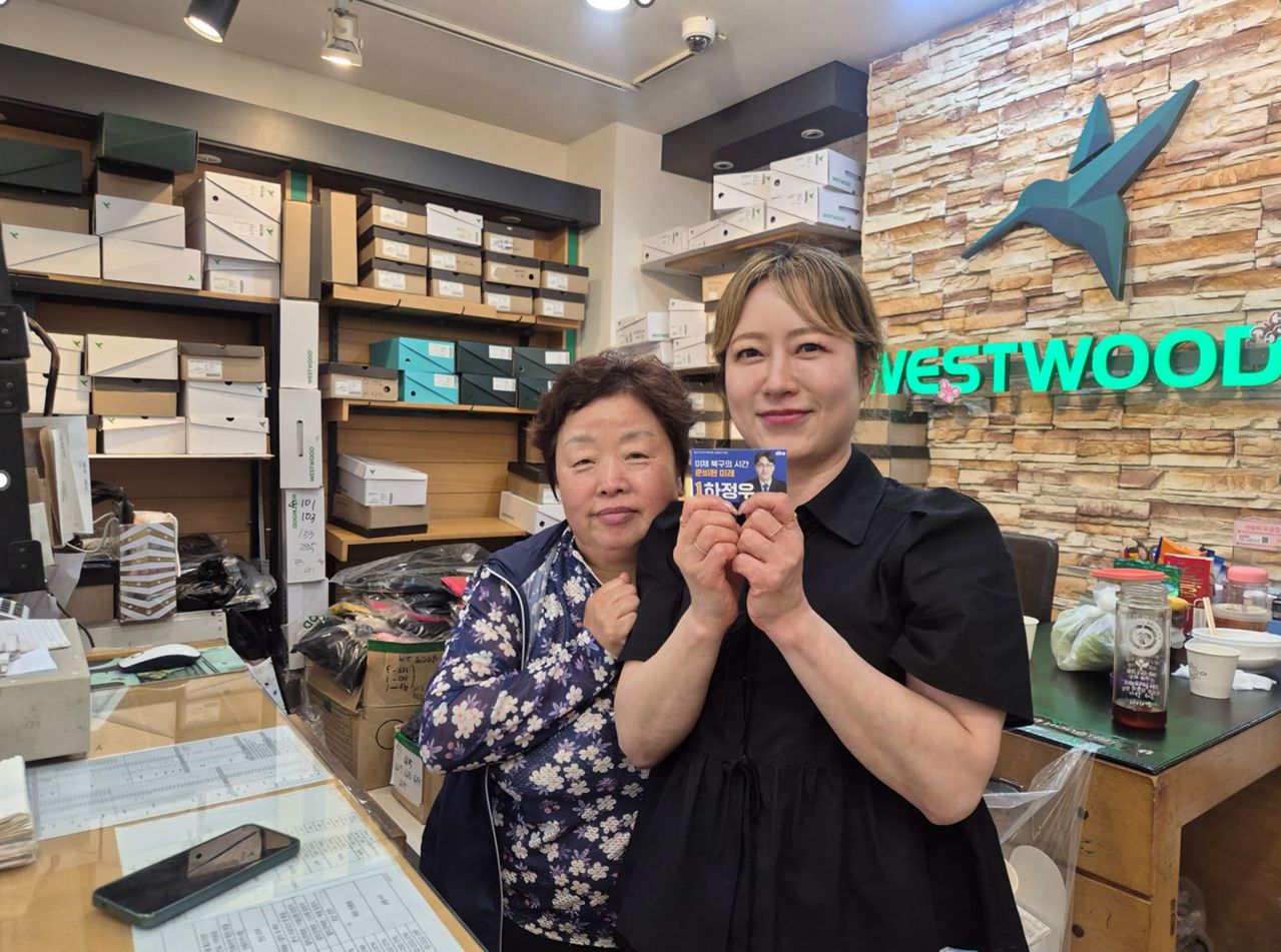 부산 북구 덕천동에서 옷가게를 운영하는 이명정(50·오른쪽)씨는 26일 ″그래도 집권여당에 힘을 실어야 한다. 하정우 후보는 우리 가게에 두 번이나 왔다″며 하 후보의 명함을 들어 보였다. 부산=오소영 기자