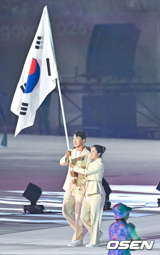 [OSEN=나고야(일본), 박준형 기자] 19일 일본 나고야 미즈호공원 육상경기장에서 제20회 일본 아이치·나고야 아시안게임 개막식이 진행됐다. 아이치·나고야 아시안게임 개회식에서 한국 선수단은 김동용·신유빈을 기수로 9개 종목 50명이 참가해 영문 국가명 순서에 따라 16번째로 입장한다. 아시안게임은 오는 10월 4일까지 열린다. 김동용과 신유빈이 한국 선수단 기수로 입장하고 있다.    2026.09.19 / soul1014@osen.co.kr