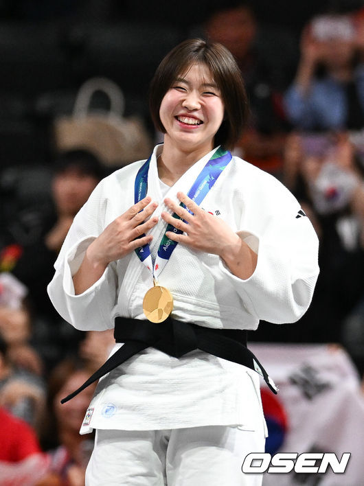 [OSEN=나고야(일본), 박준형 기자] 1일 일본 나고야 아이치 인터내셔널 아레나에서 2026년 아이치·나고야 아시안게임 유도 여자 57㎏급 결승 한국 허미미와 몽골 대표 테르비시 아리운자야의 경기가 진행됐다.허미미는 한국인 아버지와 일본인 어머니 사이에서 태어난 '재일교포'다. 복수국적자였지만, 2021년 '한국 선수로 뛰는 모습을 보고 싶다'는 할머니의 유언에 따라 한국 국적을 택했다.시상식에서 금메달 수상한 허미미가 미소 짓고 있다.  2026.10.01 / soul1014@osen.co.kr