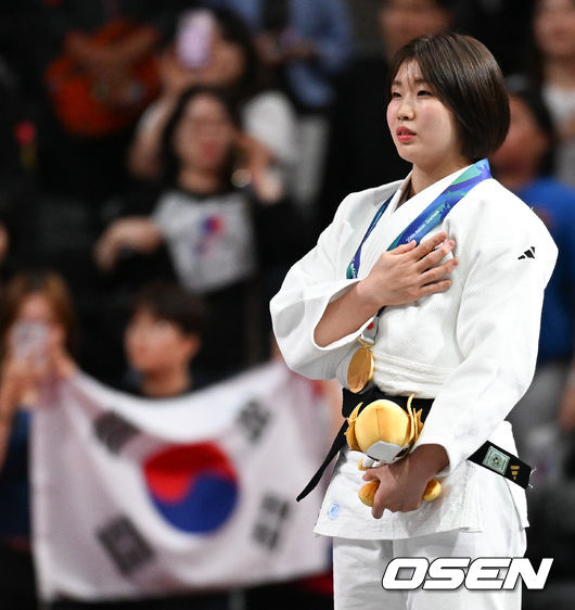 [OSEN=나고야(일본), 박준형 기자] 1일 일본 나고야 아이치 인터내셔널 아레나에서 2026년 아이치·나고야 아시안게임 유도 여자 57㎏급 결승 한국 허미미와 몽골 대표 테르비시 아리운자야의 경기가 진행됐다.허미미는 한국인 아버지와 일본인 어머니 사이에서 태어난 '재일교포'다. 복수국적자였지만, 2021년 '한국 선수로 뛰는 모습을 보고 싶다'는 할머니의 유언에 따라 한국 국적을 택했다.시상식에서 금메달 수상한 허미미가 태극기를 향해 국민의례를 하고 있다.  2026.10.01 / soul1014@osen.co.kr