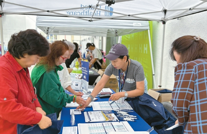 보험 에이전시 AGA 소속 에이전트들이 SMG가 함께한 가정의 달 잔치에 마련된 헬스플랜 유나이티드헬스케어(UHC) 부스에서 시니어들에게 보험 자료를 나눠주고 있다.