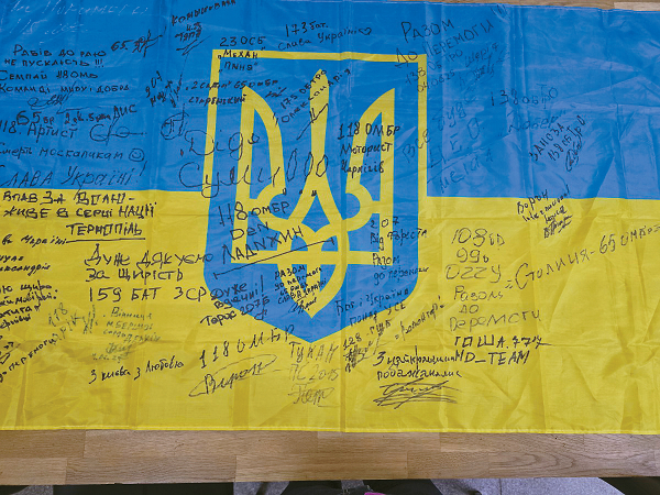 우크라이나 전선에서 임무 수행 중인 장병들이 사단법인 화랑인터내셔널에 감사의 뜻을 담아 전달한 우크라이나 국기. 부대명·고향 도시명·응원 문구가 손글씨로 적혀 있다. 