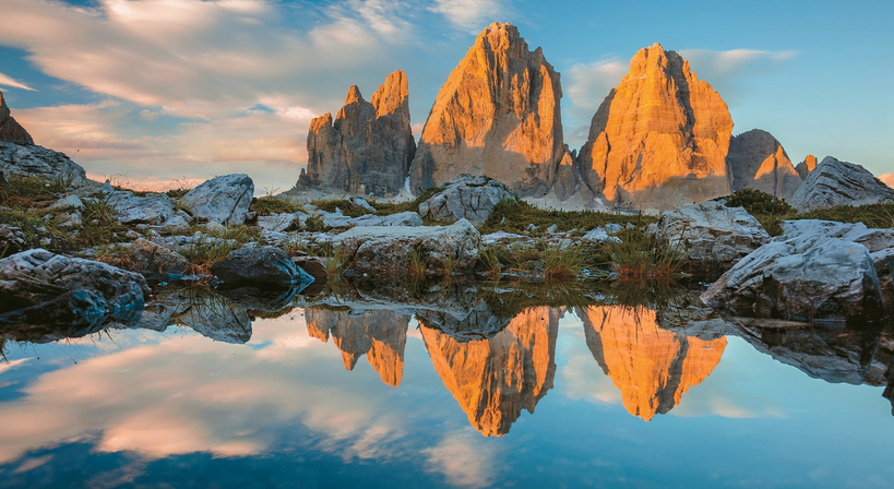 돌로미티를 대표하는 상징적 봉우리 트레 치메 디 라바레도가 석양빛에 물들고, 그 장엄한 실루엣이 고요한 호수 위에 선명하게 반영되고 있다.