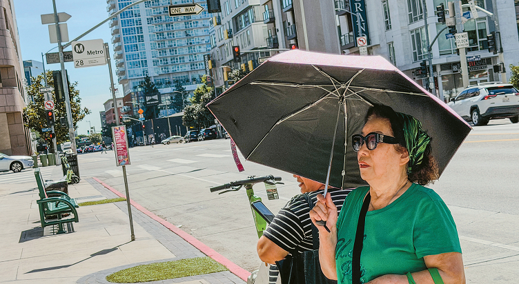 올림픽 불러바드 인근 한 버스정류장에서 한인 시니어가 그늘막이 없어 양산을 쓴 채 버스를 기다리고 있다. 김상진 기자