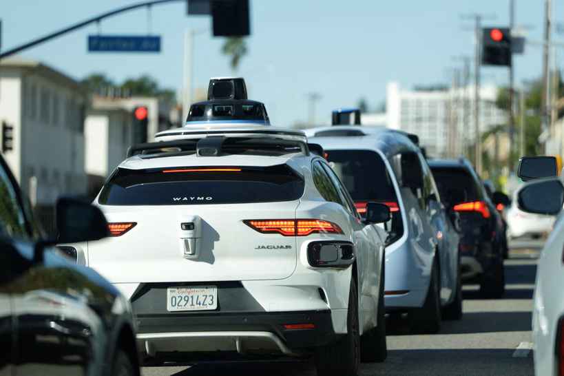 자율주행 기술을 탑재한 웨이모(Waymo) 로보택시 차량이 도심 도로에서 신호를 기다리며 일반 차량들과 함께 줄지어 서 있다.