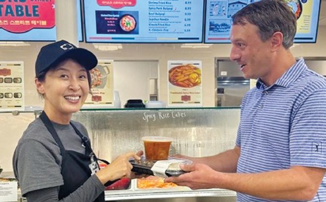 크로거 마켓 휴스턴 지점에 개장한 한식 델리 ‘라이언스 스트리트 테이블’의 스테이시 권(왼쪽) 대표가 백인 고객에게 김치찌개와 반찬을 건네고 있다. [라이언스 스트리트 테이블 제공]